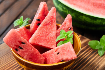 Sliced watermelon decorated with mint leaves on brown wooden background. Close-up, selective focus