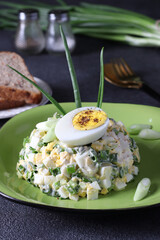 Salad with egg and green onions dressed with mayonnaise on plate on dark gray background