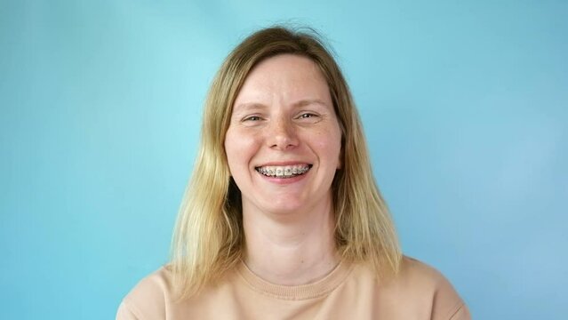Young woman with dental braces laughing isolated on blue colour background. Studio. Cute lovely girl with metal braces on white clear teeth smiling in clinic. Close Up. Positive Emotion. Stomatology.