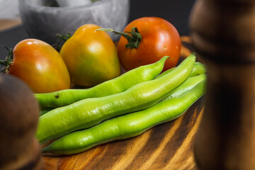 Ham toast with tomato, oil and pepper on a slate plate placed next to rustic wooden kitchen utensils, salt shaker and recipe ingredients such as tomato and broad beans