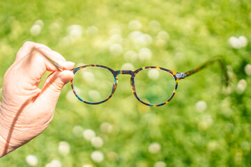 Woman with poor eyesight. Poor eyesight, hand holding stylish frame glasses on a green blurred...