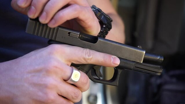 A close-up handheld camera shot showing a handgun being taken out of its bag. The man adjusts the slide lock of the gun.
