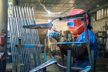 A welder in production is engaged in the manufacture of products. In a mask, in gloves, sparks fly