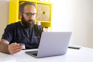 Holding credit card, young Caucasian millennial worker holding credit card and spending money online. Bearded young hipster shopping online.