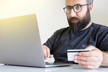 Holding credit card, bearded young caucasian man holding credit card and using laptop for online shopping.  