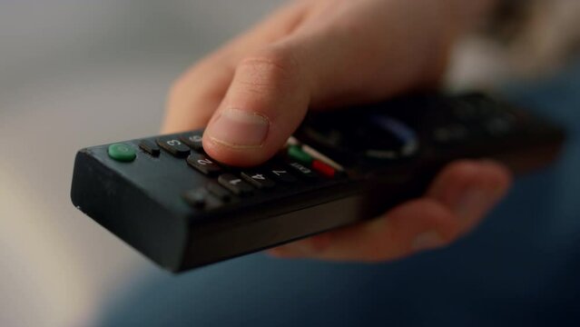 Fingers pushing remote control buttons closeup. Unknown man switching channels.