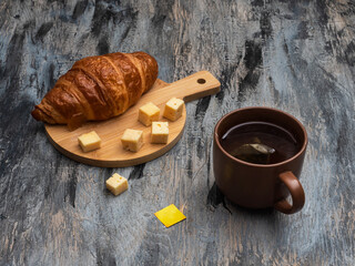 Breakfast with croissant, cheese slices and tea in a brown mug