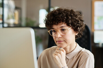 Young businesswoman in eyeglasses thinking about new ideas during her work on computer at office