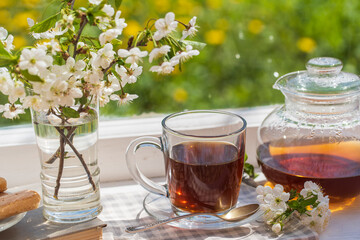 Hot tea in glass teapot and cup on windowsill at home