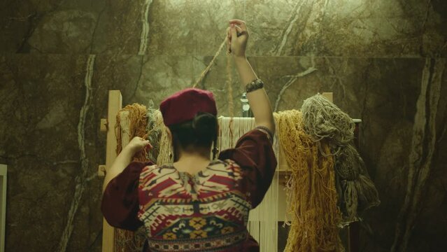 A Woman weaving traditional Asian carpet . Handmade carpet embroidery . Back view of Woman create a pattern using multi-colored threads . Rear view . Weaving machine . Needlework . Carpet-makers 