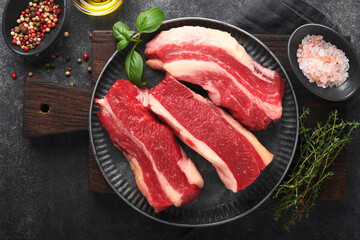 Steak beef. Raw steak New York with rosemary and spices on old iron plate on old dark stone background. Top view. Mock up.