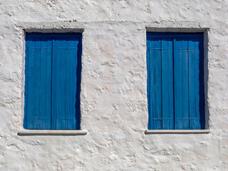 Two windows with closed blue shutters on a white-washed wall, Perdika village, Aegina island, Greece. Space for your text or logo.