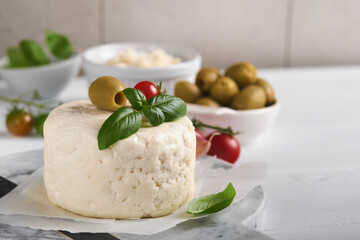Ricotta cheese. Homemade Ricotta cheese with basil, garlic, tomatoes and green olives on parchment paperback and stand on old beige tiles background. Italian food. Selective focus.