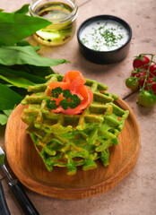 Green Belgian waffles. Spinach or wild garlic or pesto waffles with red salmon and cream sauce on old beige tile table background. Delicious breakfast, snack, brunch on old beige tiles background.