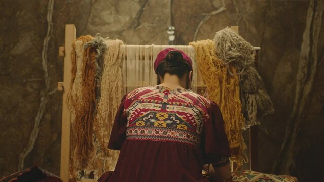 A Woman weaving traditional Asian carpet . Handmade carpet embroidery . Back view of Woman create a pattern using multi-colored threads . Rear view . Weaving machine . Needlework . Carpet-makers 