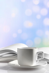 white porcelain coffee cup and saucer against the background of an open book and a blurred light background