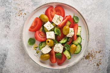 Greek salad. Fresh Greek salad with fresh vegetables, tomato, cucumber, green olives and feta cheese on old grey concrete table background. Top view.