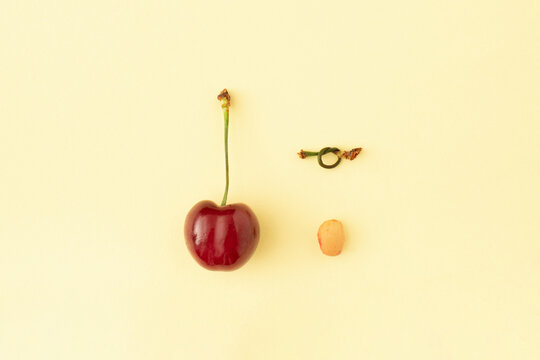 Berry stone with stalk knot and red cherry fruit on pastel background. Creative healthy food, summer fruits concept.
