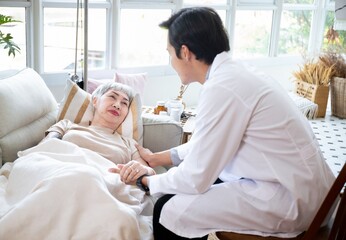 Asian Doctor Talking With Senior Female Patient In Bed At Home.Paliative care for Elder woman at home.Elderly senior patient (Asian old aging person) in nursing hospice  holding geriatrician doctor.