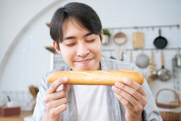 Close up of a young Handsome Asian man smelling delicious freshly baked bread at the bakery store...