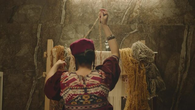 A Woman weaving traditional Asian carpet . Handmade carpet embroidery . Back view of Woman create a pattern using multi-colored threads . Rear view . Weaving machine . Needlework . Carpet-makers 