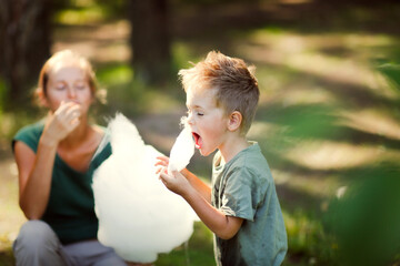 Cute european boy son and mom eating cotton candy in the park together, lifestyle