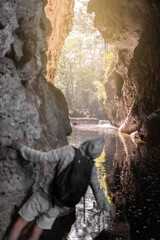 Unrecognizable man wearing a hoodie and carrying a bag is having fun watching the river passing by through a cave