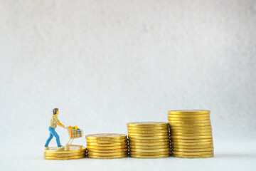 Miniature people : man go shopping / buying with cart on stack of gold coins, spending money for supermarket goods concept