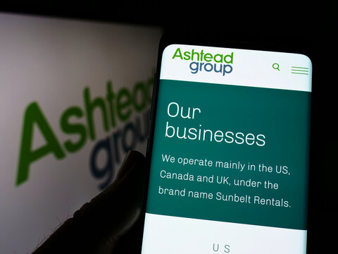 Stuttgart, Germany - 05-29-2022: Person holding cellphone with webpage of equipment rental company Ashtead Group plc on screen in front of logo. Focus on center of phone display.