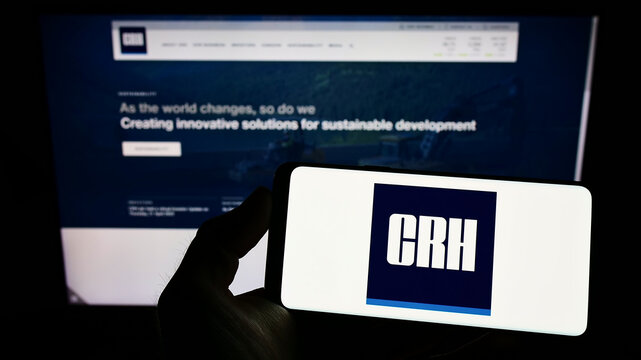 Stuttgart, Germany - 05-29-2022: Person holding smartphone with logo of Irish building materials company CRH plc on screen in front of website. Focus on phone display.