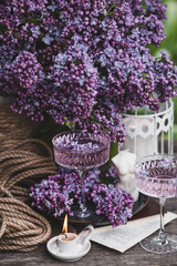A candle and fancy glasses for dessert and champagne with a lilac drink and lilac flowers inside. The fashionable shade of 2022 is very relevant. The concept of a party and a holiday. Still-life.
