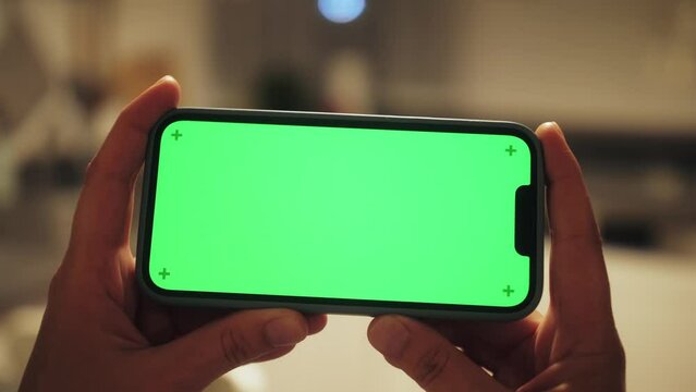 Woman using smartphone with chroma key at home. Young woman holding horizontal smartphone with green screen using streaming app watching video content in living room.