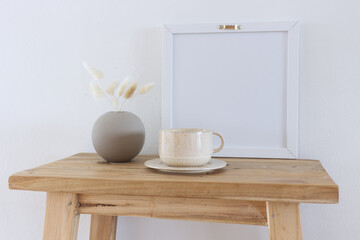 Horizontal white frame mockup on a vintage wooden bench, table. Modern ceramic vase with dry Lagurus ovatus grass. White wall background. Scandinavian interior. Selective focus.