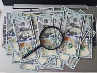 Magnifying glass and dollar bills on laptop closeup