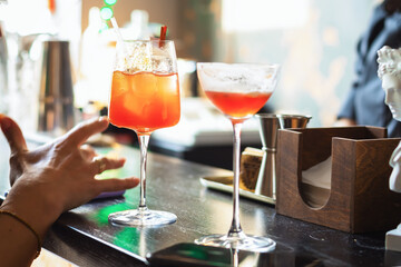 two glasses with an unfinished cocktail.  a woman's hand with a phone. close-up. bar counter