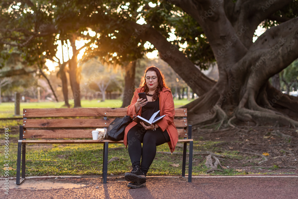 Fototapete an executive plus-size woman working outdoors. she is holding a notebook and sending a text message 