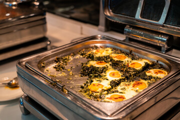 Breakfast buffet food in heating trays in hotel restaurant with eggs with spinach