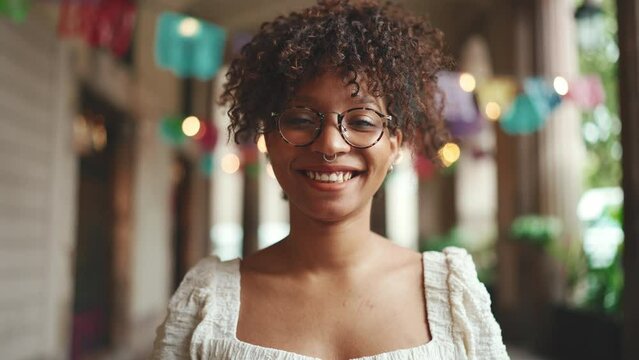 Closeup portrait of a young woman in glasses smiling posing on smartphone selfie camera. Positive woman using mobile phone outdoors in urban background.