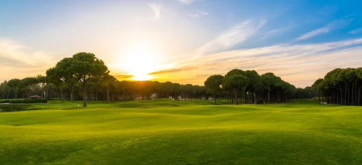 Stoff pro Meter Golf course at sunset with beautiful blue sky. Scenic panoramic view of perfect golf fairway. Golf field with high pines © SDF_QWE