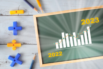 New year 2022 to 2023 and growth graph written on chalkboard with mathematics symbol and colored pencil on wooden desk. Business startup return on investment success concept and making money idea