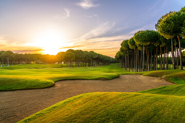 Golf course at sunset with beautiful sky and sand trap. Scenic panoramic view of golf fairway with...