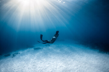 Freediver woman with fins glides on deep in ocean. Free diver and sunlight underwater