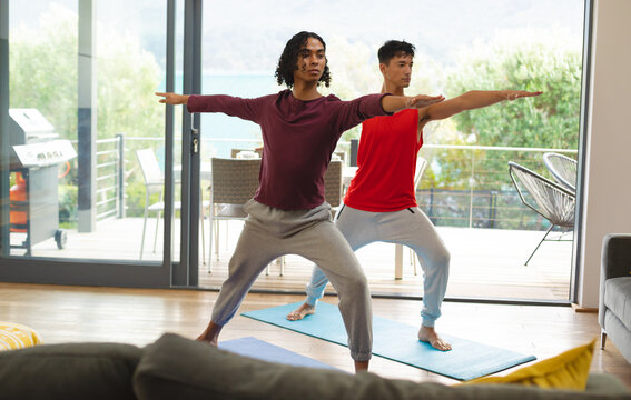 Diverse gay male couple practicing yoga together in the living room at home