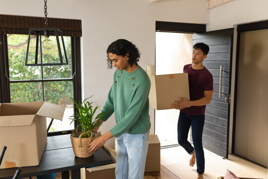 Diverse gay male couple unpacking cardboard boxes together at new home