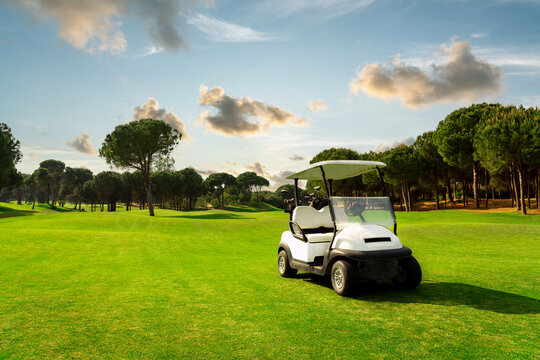 Golf cart in fairway of golf course with green grass field with cloudy sky and trees at sunset in Belek, Turkey