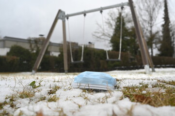 Surgical mask lying on snow-covered ground with a swing in the background