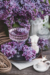 Obraz premium A candle and fancy glasses for dessert and champagne with a lilac drink and lilac flowers inside. The fashionable shade of 2022 is very relevant. The concept of a party and a holiday. Still-life.