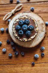 Delicious tartlet with fresh blueberries and chocolate, on wooden background. Trendy dessert. Top view