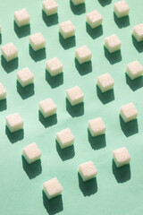 Refined sugar on green background.Cubes of sweet and white sugar in geometricshape. Hard shadows.