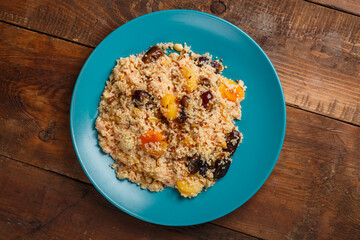 A large dish of couscous with dried fruits, saffron and nuts on a wooden table.